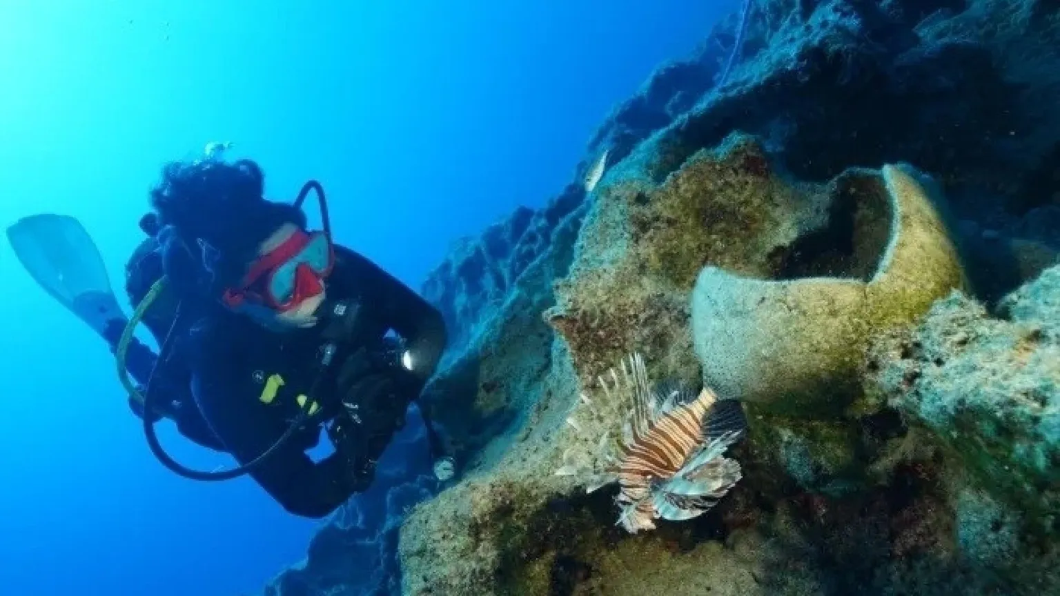 Una donna con muta da sub esplora un fondale marino dove ci sono resti di anfore