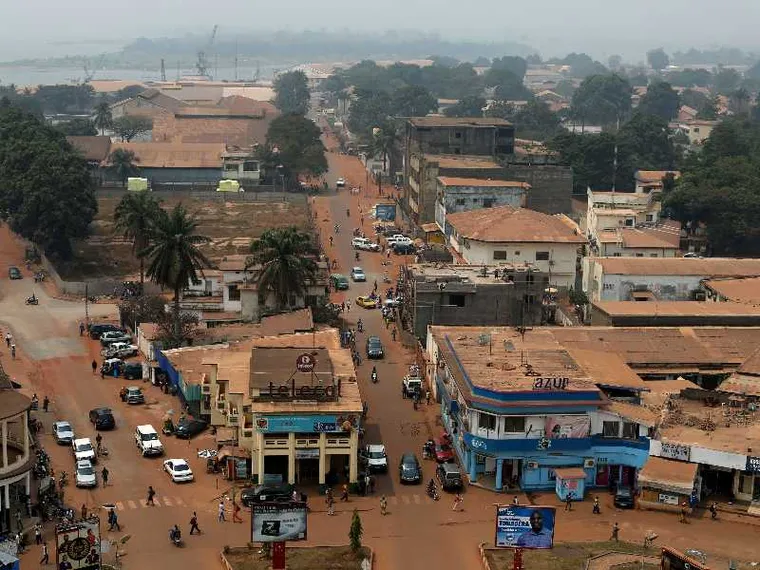 Una strada in terra battuta attraversa la capitale della Repubblica Centrafricana, Bangui. Gli edifici appaiono come fatiscenti. Il colore dominante è l'arancione.