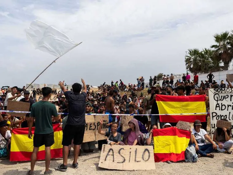 Migranti sventolano bandiere spagnole e cartelli con la scritta "Asilo" nell'exclave di Ceuta