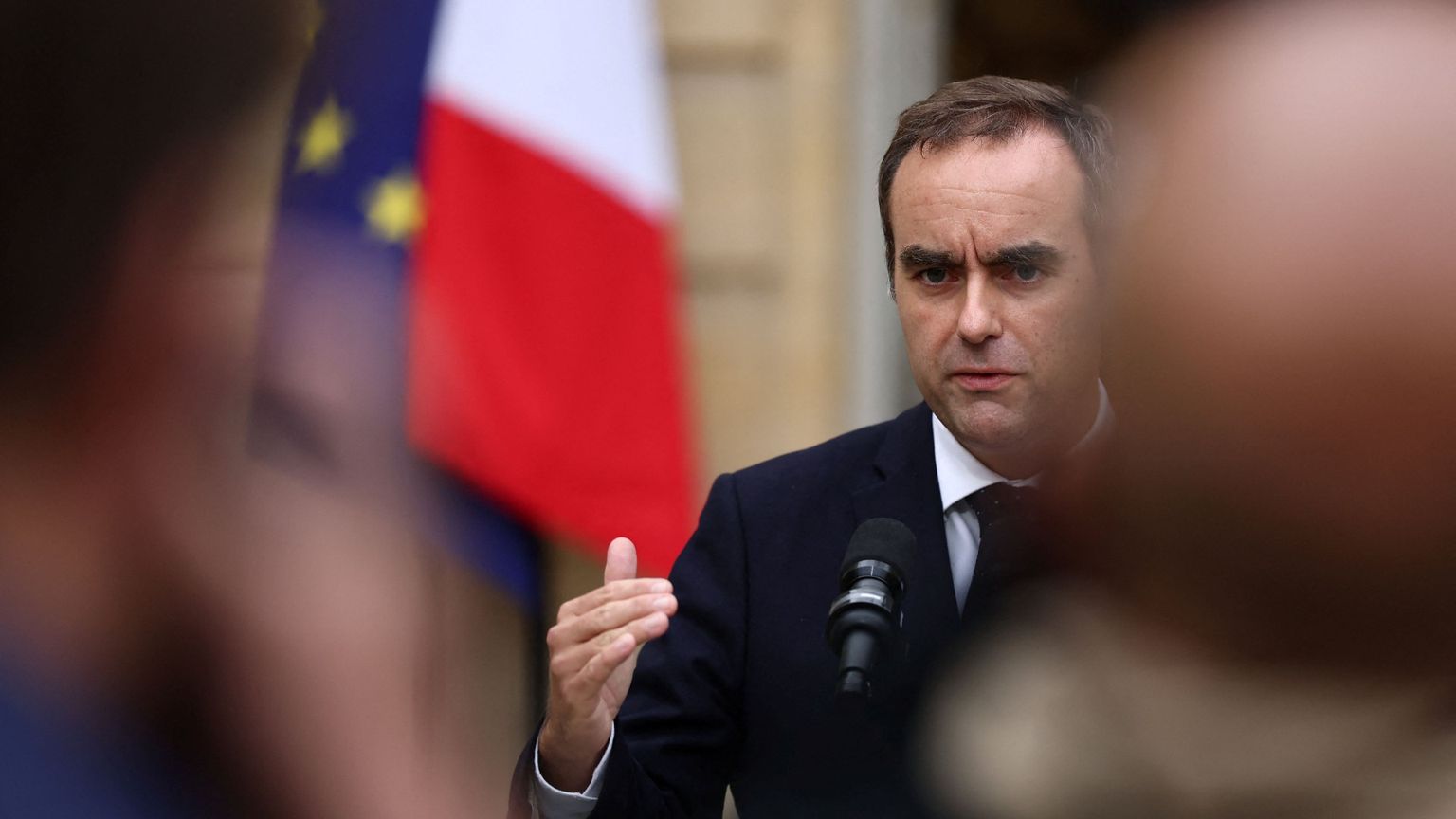 Sebastien Lecornu davanti a un microfono, con un'espressione tesa, la fronte corrugata. Alle sue spalle le bandiere francese e dell'Ue