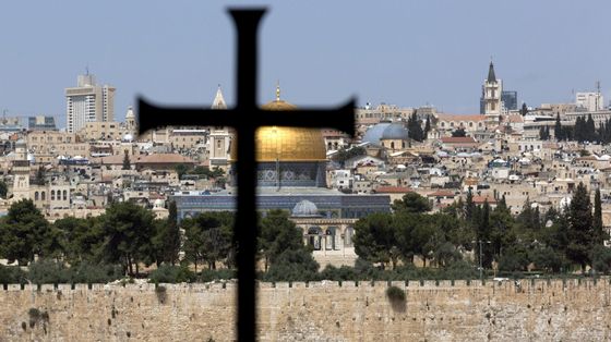 Una grande croce latina in primo piano, davanti al muro che cinge la Città Vecchia e oltre il quale spiccano l'oro della Cupola della Roccia, le cupole più basse del Santo Sepolcro e un campanile