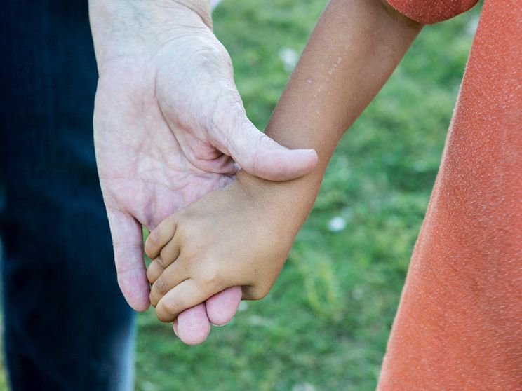 Due mani che si stringono: quella di un adulto e di un bimbo adottato