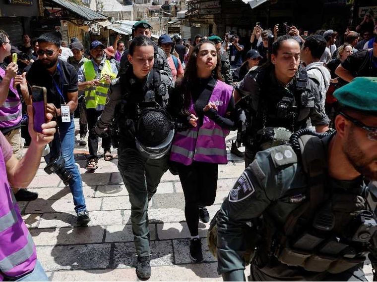 Una ragazza con un giubbino catarifrangente rosa, indossato dagli attivisti di "Standing Together", portata via da due poliziotte in mezzo a una manifestazione