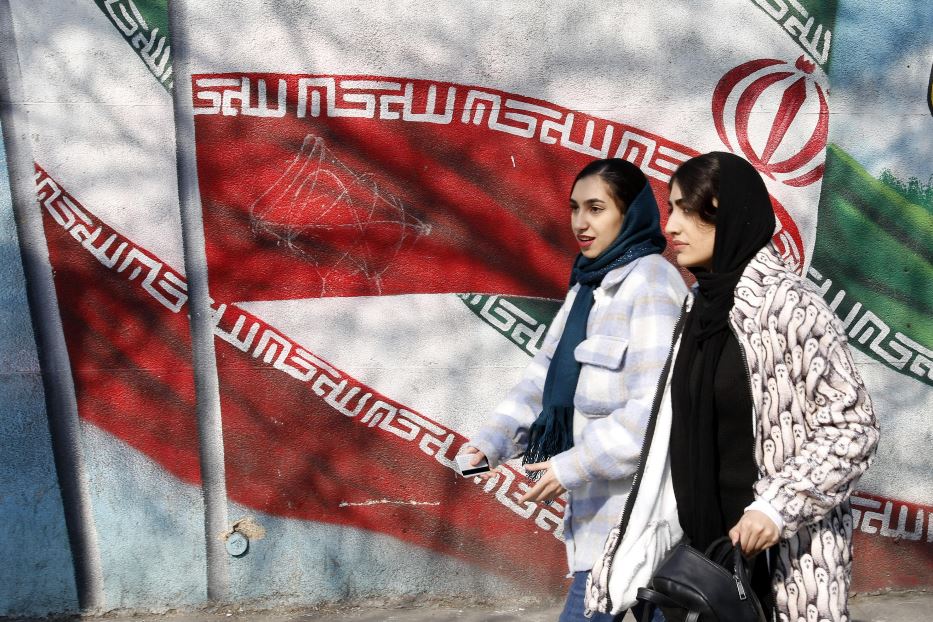 Due ragazze mentre passeggiano di fronte al murale con la bandiera dell’Iran lungo le strade di Teheran