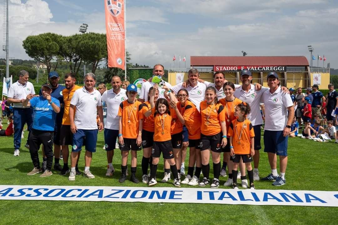 Le ragazze arancionero della Dimateam a Coverciano durante la Junior Cup, mentre sollevano il trofeo dell'Associazione italiana calciatori.