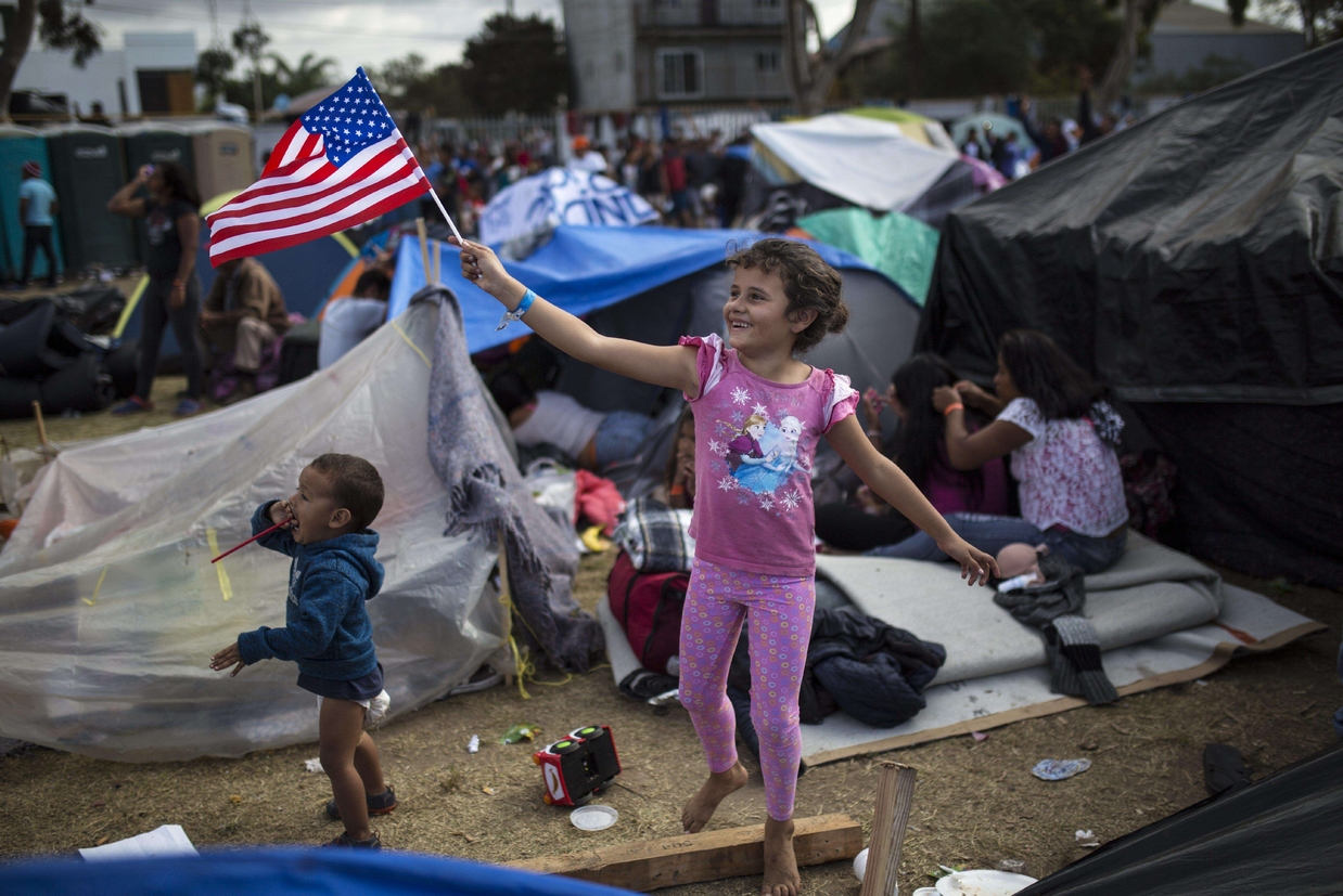 Genesis Belen Mejia Flores, 7 anni, dell'Honduras, sventola la bandiera statunitense sorridendo agli elicotteri della polizia Usa che sorvolano il Centro sportivo Benito Juarez a Tijuana, che accoglie i migranti centroamericani (Ansa) - 