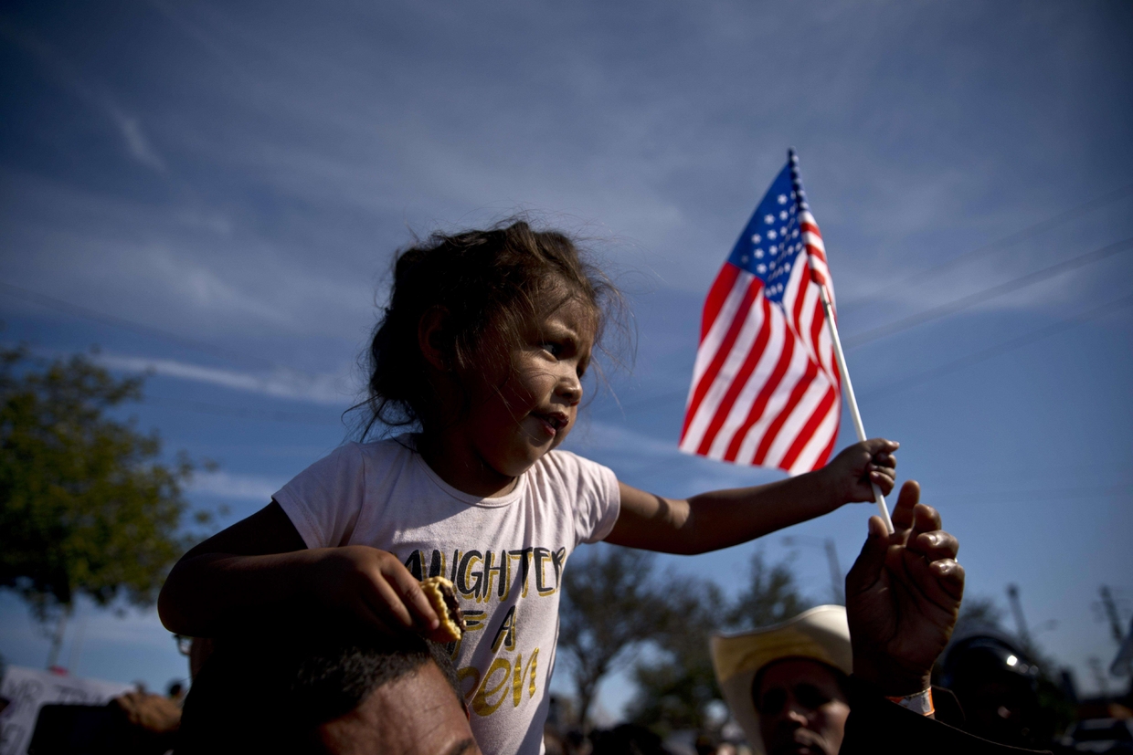 Una bambina sventola la bandiera Usa, durante la marcia dei migranti verso la frontiera di Chaparral a Tijuana (Ansa) - 