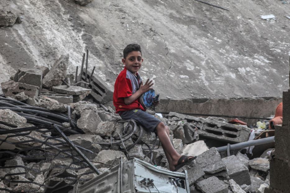 Bambino palestinese a Gaza, seduto sulle rovine della sua casa distrutta dai raid israeliani