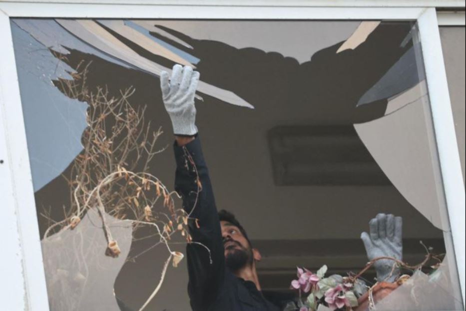 Un poliziotto raccoglie frantumi di vetro da una finestra dell'edificio colpito da un drone a Tel Aviv