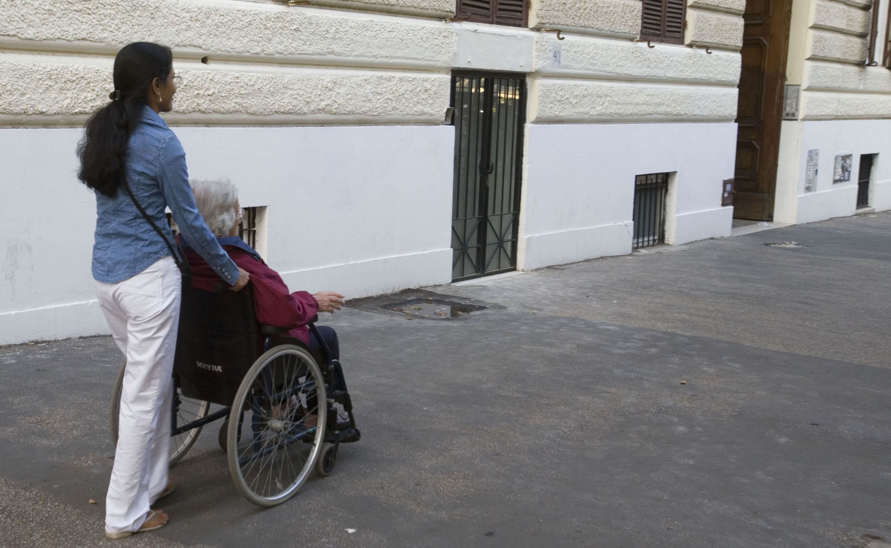 Una badante spinge un'anziana in sedia a rotelle