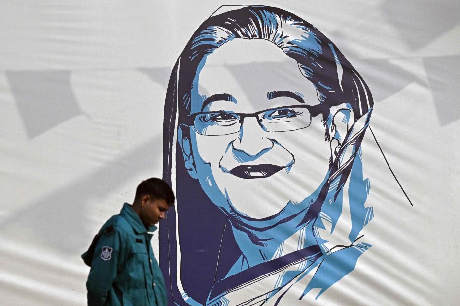Un poliziotto passeggia davanti a un muro nella capitale Dacca con il ritratto della ormai ex premier Sheikh Hasina Wazed